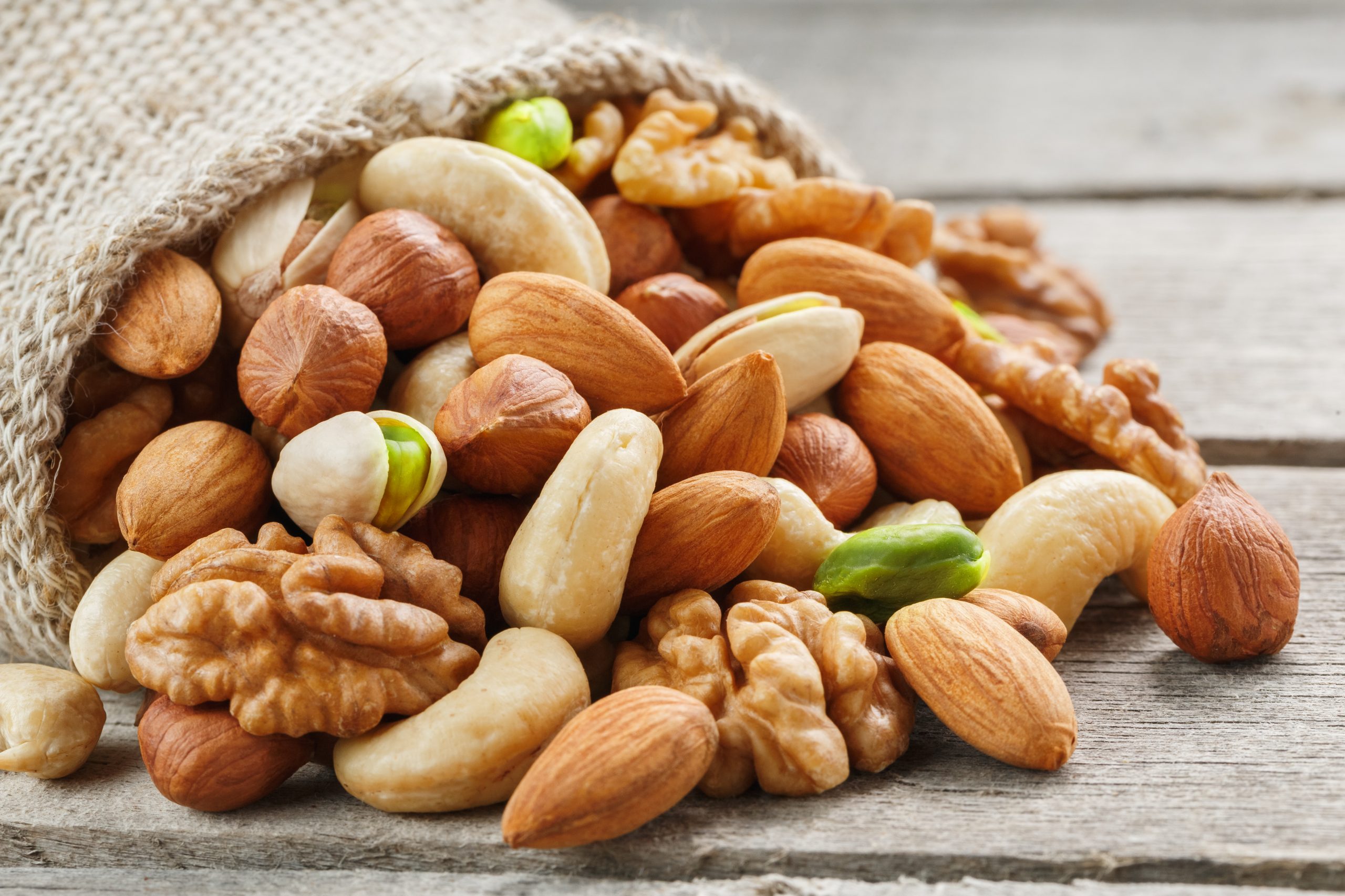 Mix of nuts of cashew, almonds, pistachios, hazelnuts and walnuts is against the background of brown fabric of burlap. Nuts as structure and background, macro